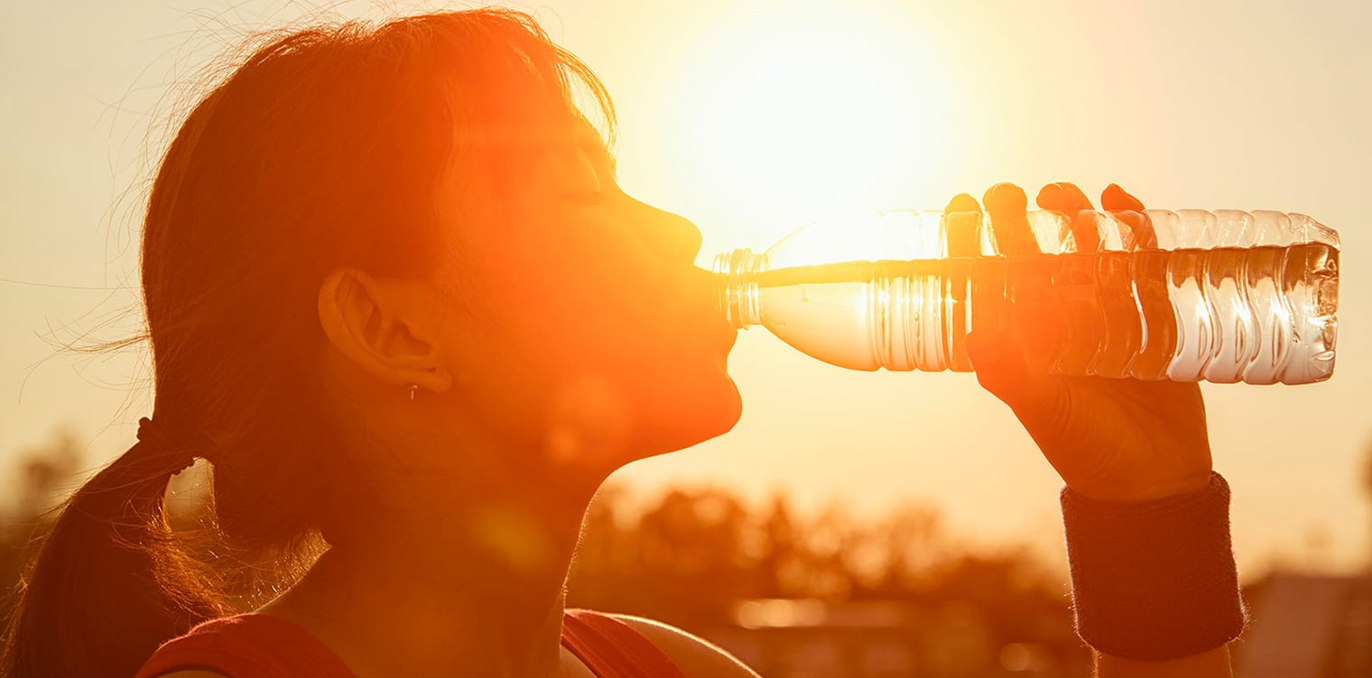 Jolie photo artistique d une femme buvant de l eau d une bouteille - comment eviter le coup de chaleur d exercice | IK Paris