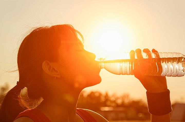 Femme buvant d une bouteille d eau pendant le coucher du soleil - coup de chaleur exercices soportif | IK Paris