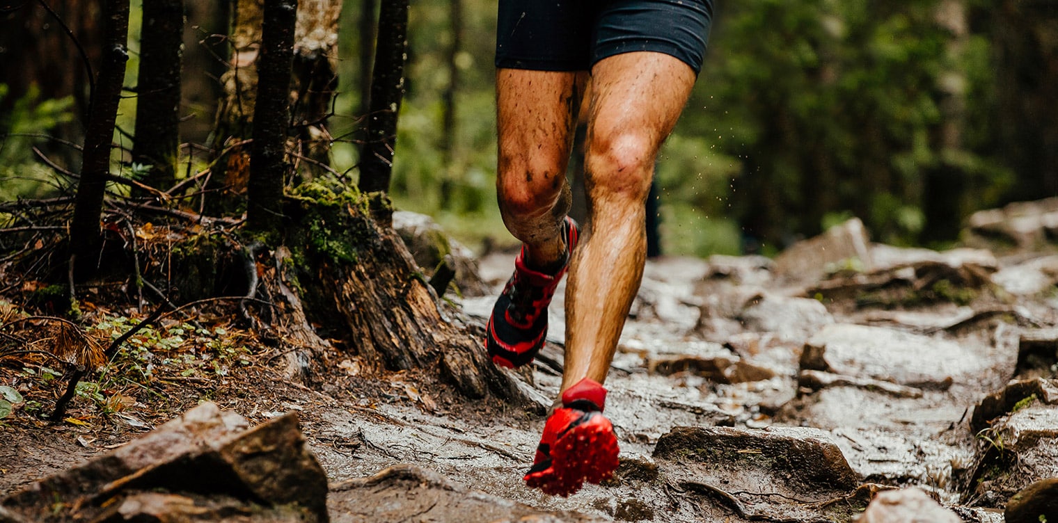 Photo des pieds d un homme qui court dans une foret - conseils pour bien debuter le trail running | IK Paris